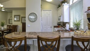 Une cuisine avec un plan de travail en granit, des chaises en bois, une horloge et une porte blanche.