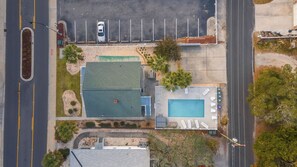 An aerial view of a property with a swimming pool, a parking lot, and a building with a green roof.