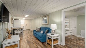 A room with a blue sofa, a white side table with a lamp, a wooden dining table with chairs, and a television mounted on the wall. - 2 story, 2nd Row House w/private pool & hot tub + Free Attraction Tickets! (North Myrtle Beach)