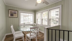 A dining area with a glass table and white chairs, large windows with blinds, and a ceiling fan. - 2 story, 2nd Row House w/private pool & hot tub + Free Attraction Tickets! (North Myrtle Beach)