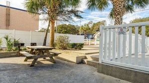 A picnic table with benches, a white fence, and a sign prohibiting glass containers in the pool area.