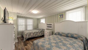 A bedroom with two beds, a dresser, a vanity, and a window with blinds.