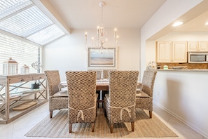 A dining area with a chandelier, woven chairs, and a table with a glass top.