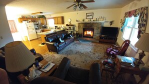 Una sala de estar con chimenea, televisor y una cocina al fondo.