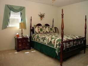 Una cama con dosel, un edredón, una mesita de noche con lámpara y una ventana con cortinas.