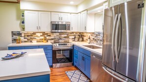 A modern kitchen with white cabinets, a stainless steel refrigerator, a microwave, and a stove.