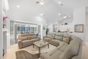 A spacious living area with a large sofa set, a coffee table, and a view of the outdoors through a glass door.