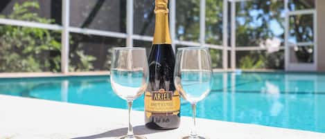 Una botella de champán Ariel Brut Cuvée y dos copas sobre una mesa junto a la piscina.