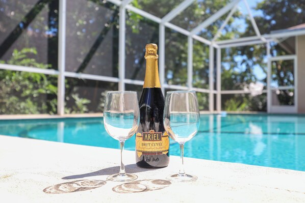 A bottle of Ariel Brut Cuvée champagne with two glasses on a poolside table.