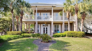 A two-story building with a balcony, a covered entrance, and a well-maintained garden with palm trees and shrubs.