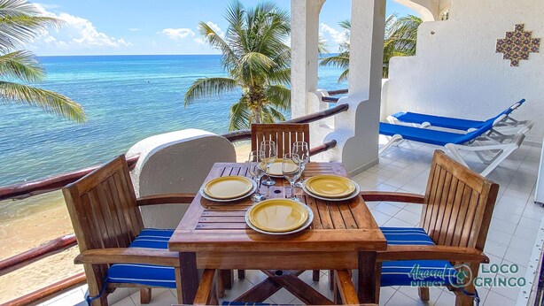 A wooden table set for four with plates and glasses, overlooking a beach with palm trees and the ocean. - Spacious with beautiful upper level views of Half Moon Bay! (Akumal)