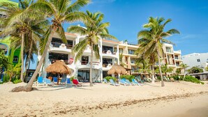 A beachfront hotel with multiple balconies, palm trees, and beach chairs. - Spacious with beautiful upper level views of Half Moon Bay! (Akumal)