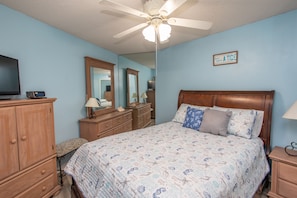 A bedroom with a bed, a dresser, a vanity with a mirror, a television, and a ceiling fan. - FEELS LIKE HOME IN THIS GORGEOUS 2 BEDROOM OCEANFRONT CONDO (MURRELLS INLET)