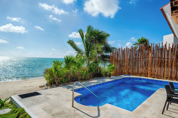 A swimming pool with a view of the ocean, surrounded by tropical plants and a wooden fence.