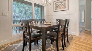 A dining area with a wooden table and chairs, large windows, and a chandelier. - Completely Renovated, 5 min walk to beach (Kiawah Island)