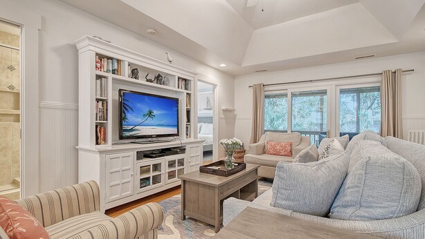 A spacious living room with a large flat-screen TV, a bookshelf, a comfortable sofa, and a dining area. - Completely Renovated, 5 min walk to beach (Kiawah Island)