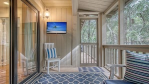 A covered porch with a patterned floor, a television mounted on the wall, and a view of the outdoors through the windows. - Completely Renovated, 5 min walk to beach (Kiawah Island)