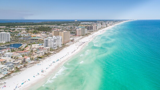 A coastal cityscape with a long sandy beach, high-rise hotels, and a clear blue sea.