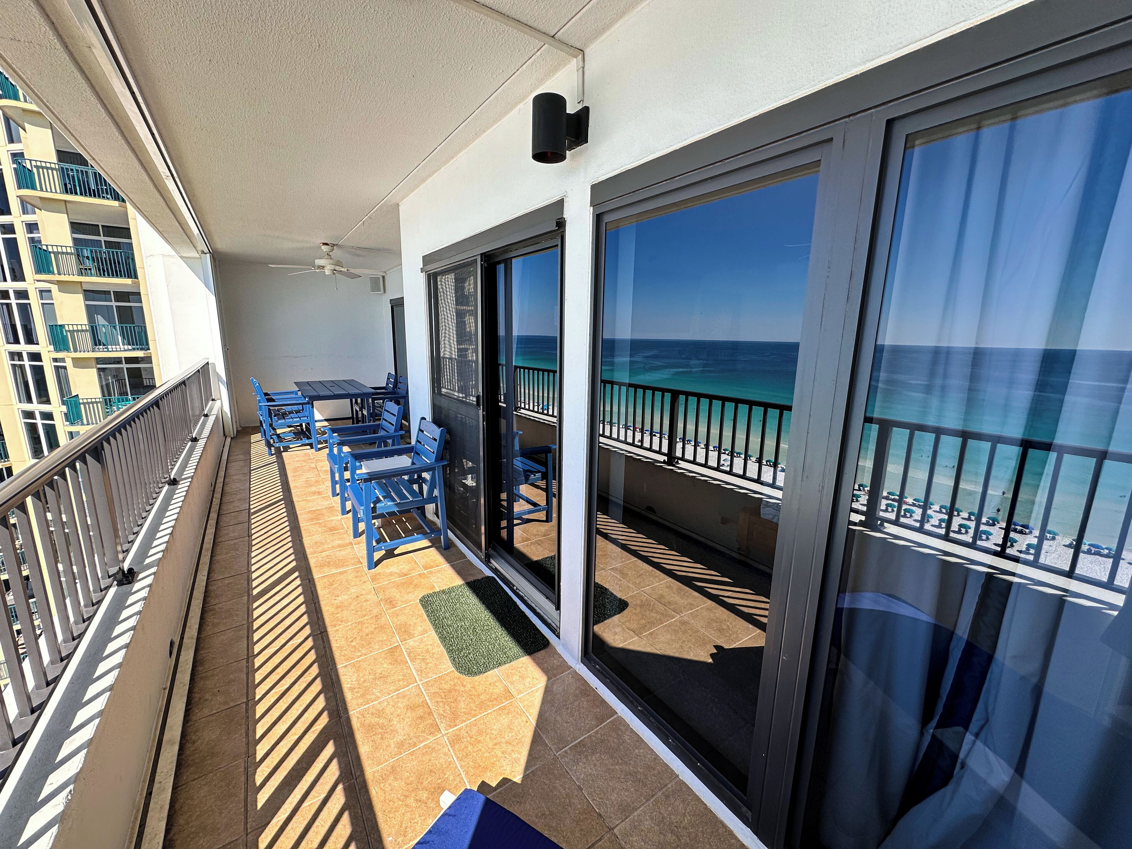 A balcony with blue chairs and a table, overlooking a beach with a clear view of the ocean.