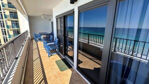 A balcony with blue chairs and a table, overlooking a beach with a clear view of the ocean.