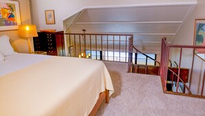 Ein Schlafzimmer mit einem großen Bett, einem Nachttisch, einer Lampe, einer Kommode und einem Fenster mit Blick ins Freie.