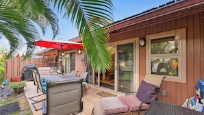 Un espace patio aménagé avec du mobilier d’extérieur, un coin salon abrité et une porte-fenêtre coulissante donnant sur un espace intérieur.