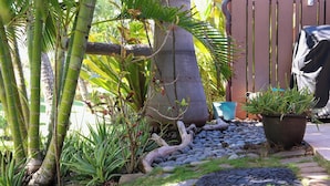 Un jardin avec des bambous, un grand tronc d’arbre, une plante en pot et un chemin de pierres.