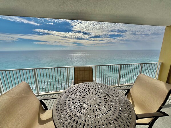 A balcony with a round table and two chairs, overlooking a turquoise sea and a clear sky.