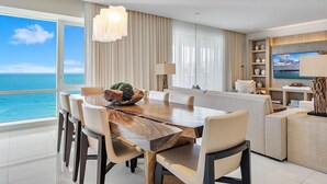 Een moderne eetruimte met een grote houten tafel, meerdere stoelen en uitzicht op de oceaan door grote ramen.