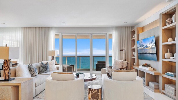 Een moderne woonkamer met een groot raam met uitzicht op zee, een flatscreen televisie en een houten boekenplank.