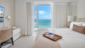 Hotelkamer met een bed, bureau, stoel, dienblad met glazen en een karaf, en uitzicht op de oceaan.