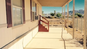 A covered outdoor area with a concrete floor, a wooden staircase, and a view of a desert landscape with mountains in the background.
