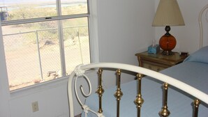 A bedroom with a metal bed frame, a bedside table with a lamp, and a window with a view of a landscape.
