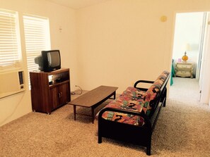A living room with a sofa, a television on a wooden cabinet, a coffee table, and a carpeted floor.