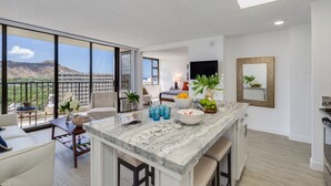 Un apartamento moderno con cocina, comedor y sala de estar. Cuenta con ventanas amplias, un televisor de pantalla plana y un balcón con vistas a las montañas.