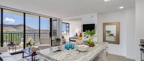 A modern apartment with a kitchen, dining area, and living room. It features large windows, a flat-screen TV, and a balcony with a view of the mountains.