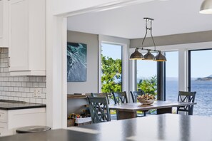 Uma cozinha moderna com uma ilha grande, um espaço de refeições com vista para o mar e um quadro na parede.