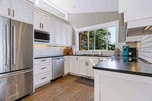 A modern kitchen with white cabinetry, stainless steel appliances, and a large window offering a view of trees. - UNIQUE RESIDENTIAL OCEANFRONT PROPERTY ON VANCOUVER ISLAND (Nanoose Bay)