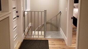 A narrow hallway with a wooden floor, a black rug at the entrance, a white door on the left, and a staircase with a white railing leading to a bedroom. - UNIQUE RESIDENTIAL OCEANFRONT PROPERTY ON VANCOUVER ISLAND  (Nanoose Bay)