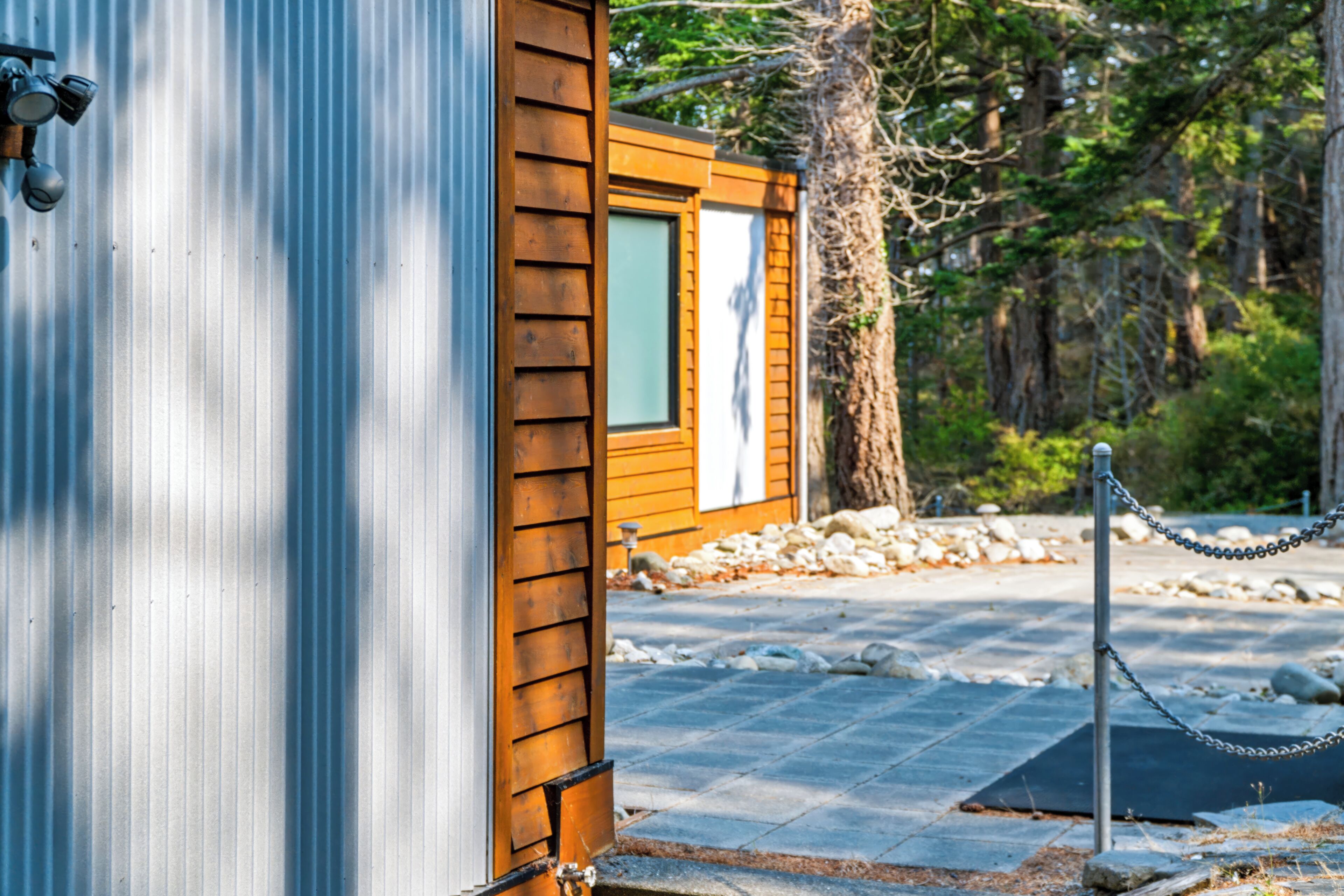 A wooden cabin with a metal exterior, a window, and a paved area with stones and a chain-link fence.
