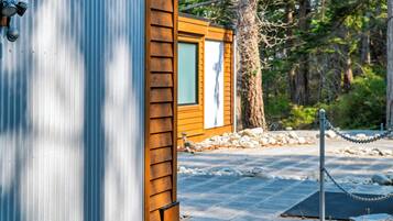 A wooden cabin with a metal exterior, a window, and a paved area with stones and a chain-link fence.