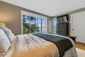Quarto com cama grande, cômoda, televisão e vista para o exterior.