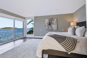 A bedroom with a large bed, a painting, and a view of the sea. - UNIQUE RESIDENTIAL OCEANFRONT PROPERTY ON VANCOUVER ISLAND  (Nanoose Bay)
