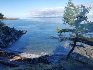 Un paisaje costero con una costa rocosa, agua cristalina y una cadena montañosa distante.