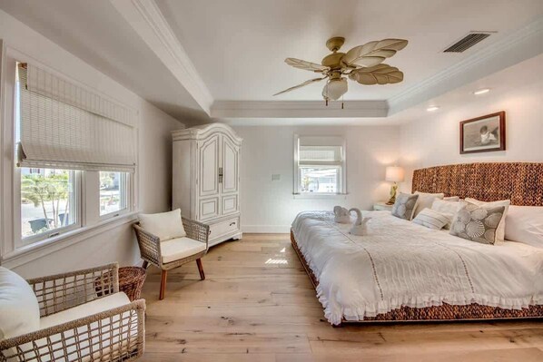 A bedroom with a large bed, a ceiling fan, a wardrobe, and a window with blinds.