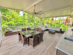 A covered outdoor area with a dining table, seating, and a ceiling fan.