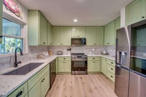 A kitchen with green cabinets, a stainless steel refrigerator, a double oven, and a window with a view.