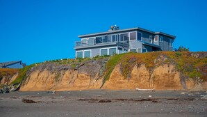 Een modern huis met twee verdiepingen en een balkon, gelegen op een rotsachtige klif met uitzicht op een strand.