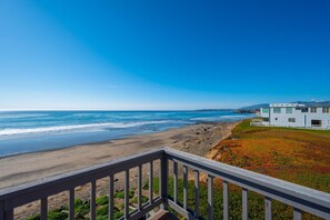 A coastal view from a balcony overlooking a beach and ocean, with a modern house in the background.