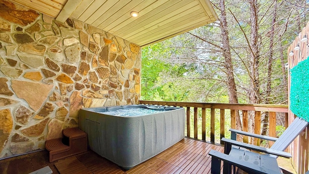 A stone-walled hot tub area with wooden decking and outdoor furniture. - Beautiful mountain cabin (Sevierville)